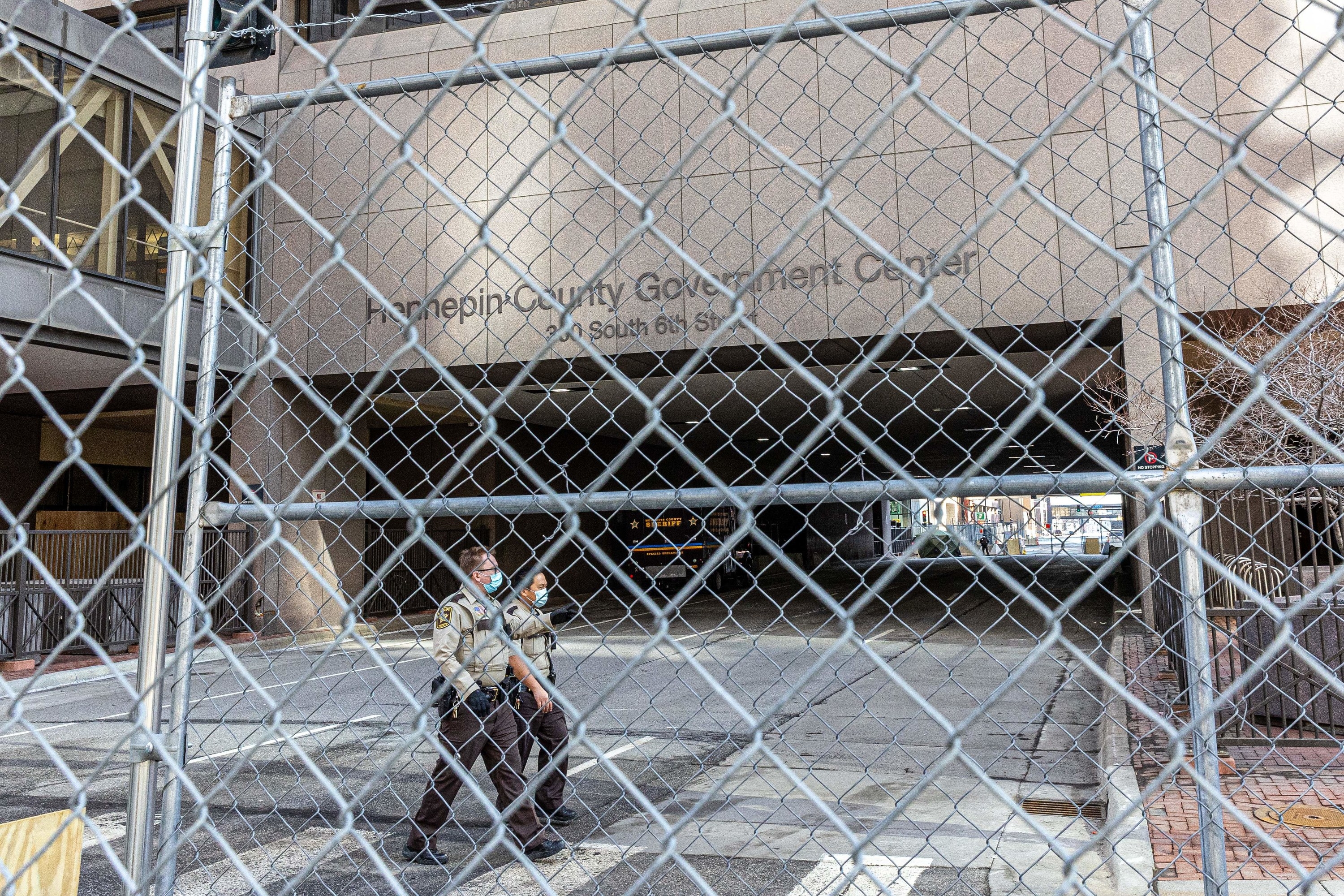 Masked police officers walk between fencing and the Hennepin County Government Center