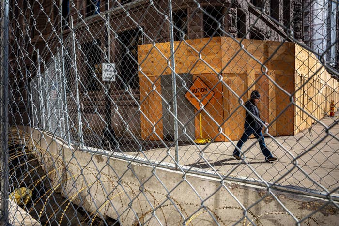 A person walks between the city hall building and a metal fence