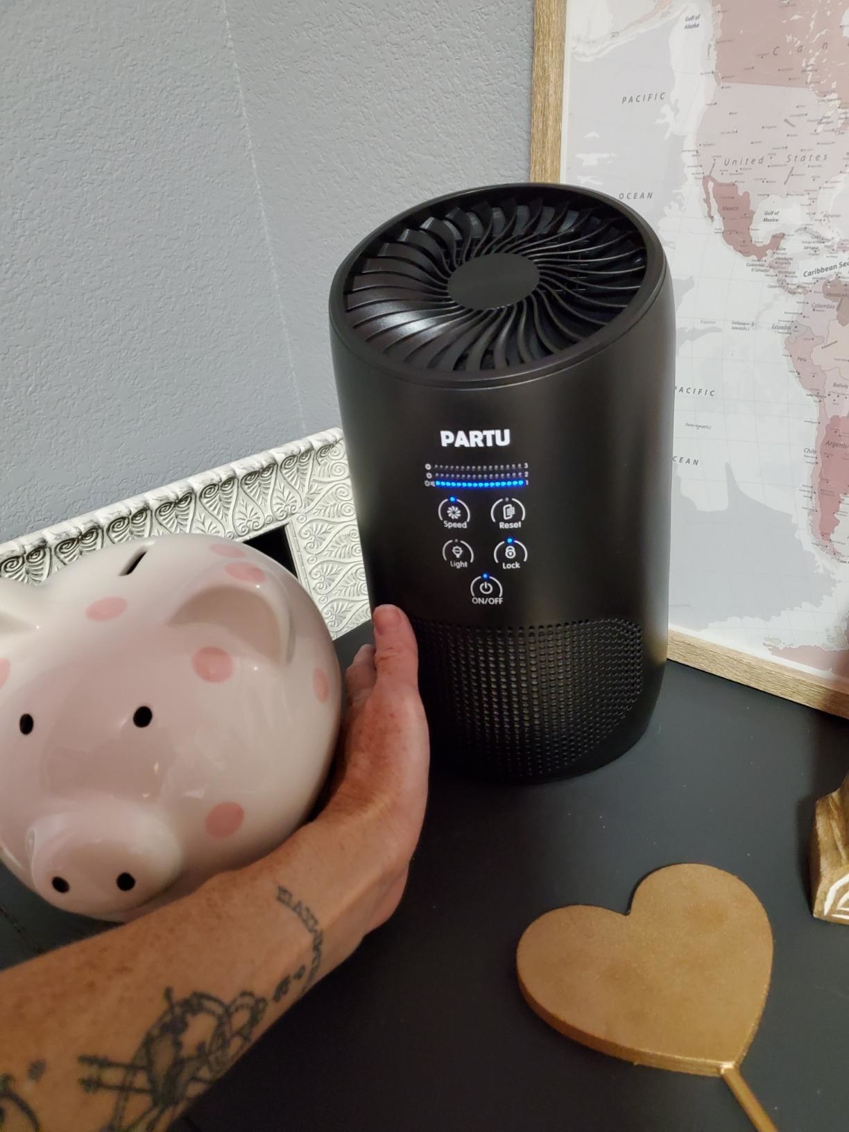 reviewer shows small black humidifier on dresser next to pink piggy bank 