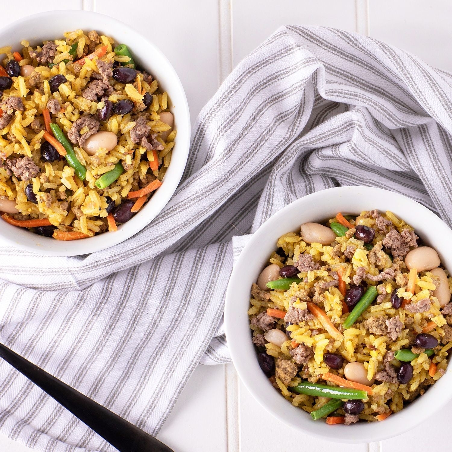 Two bowls of golden rice dotted with ground beef, beans, and carrots