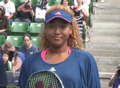 Naomi Osaka posing for photos with her tennis racket