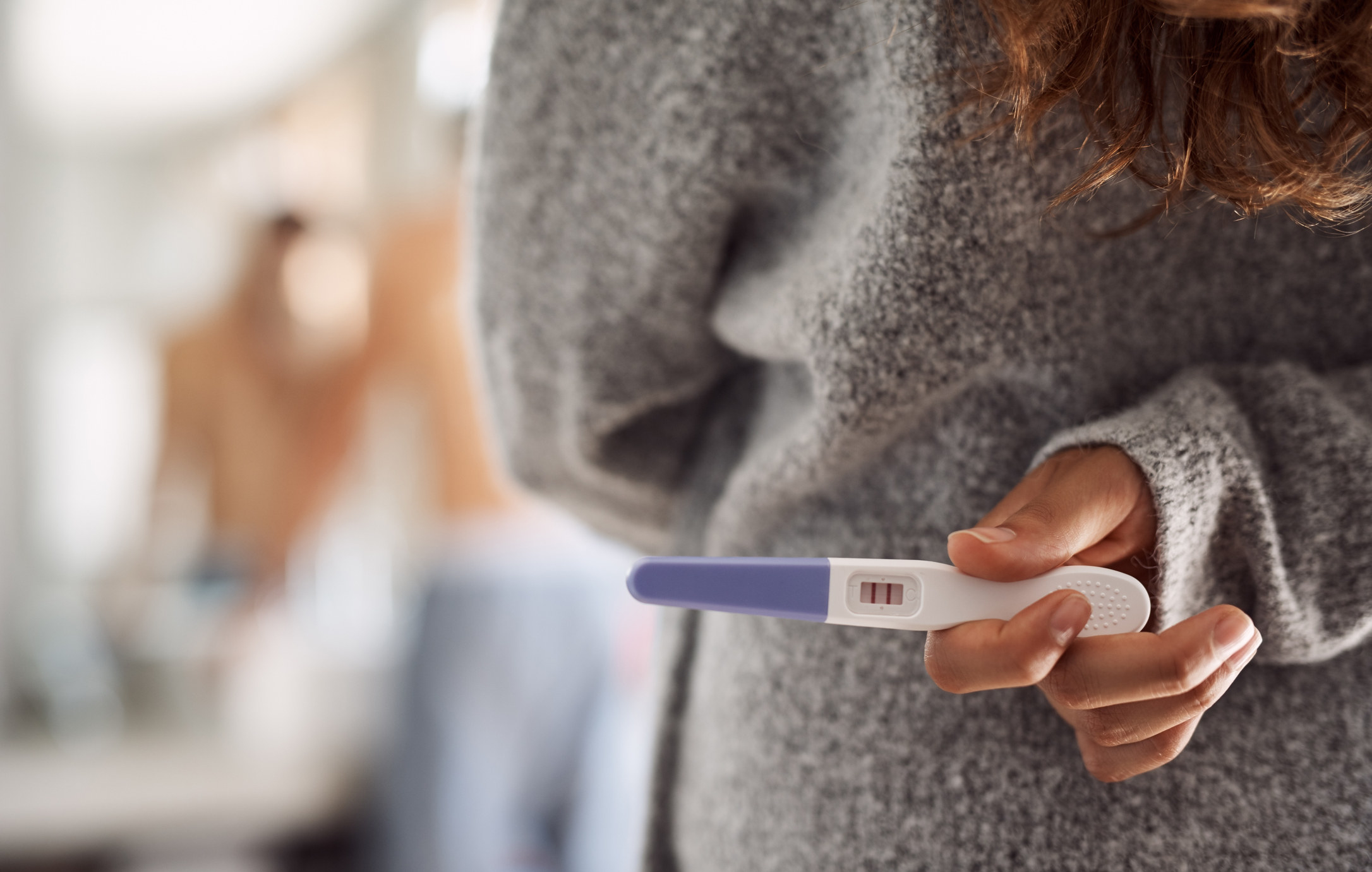 a woman holding a pregnancy test behind her back