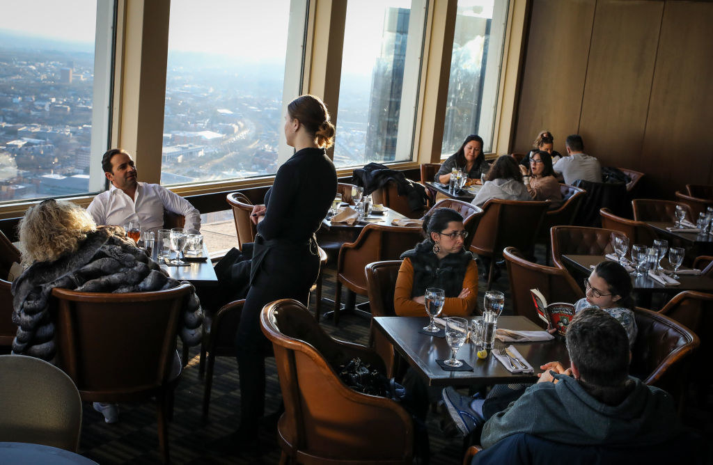 A waitress speaks to a two people sitting at one of the tables in a busy restaurant