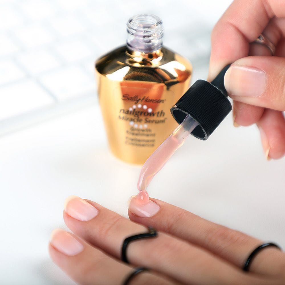 A person using a dropper tool to apply serum to their nails