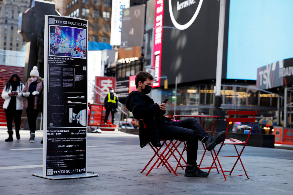 A mostly empty Times Square with a few people wearing face masks