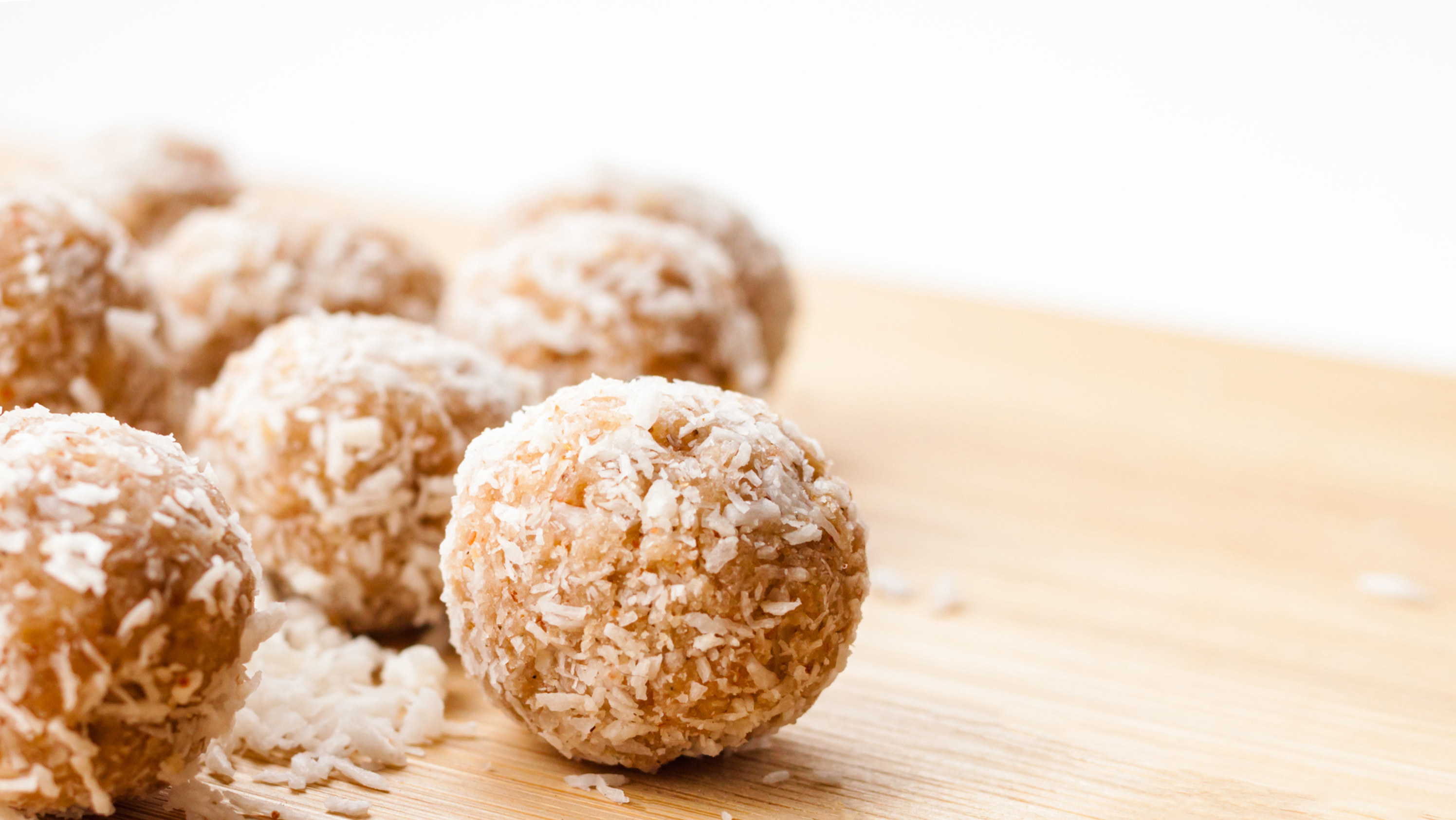 Coconut coated bliss balls on a wooden chopping board 
