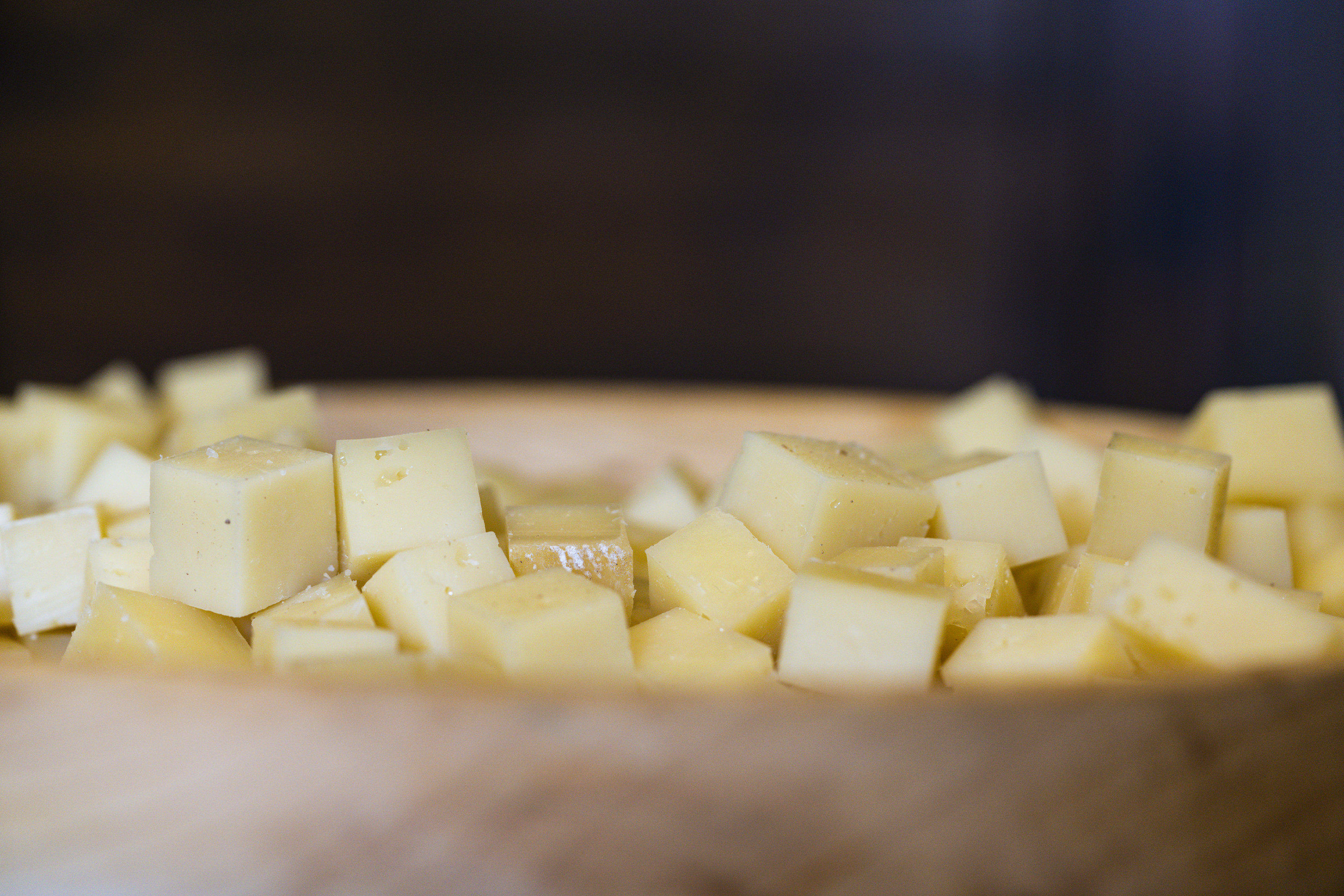 A close up of cheese cut into cubes in a wooden bowl 