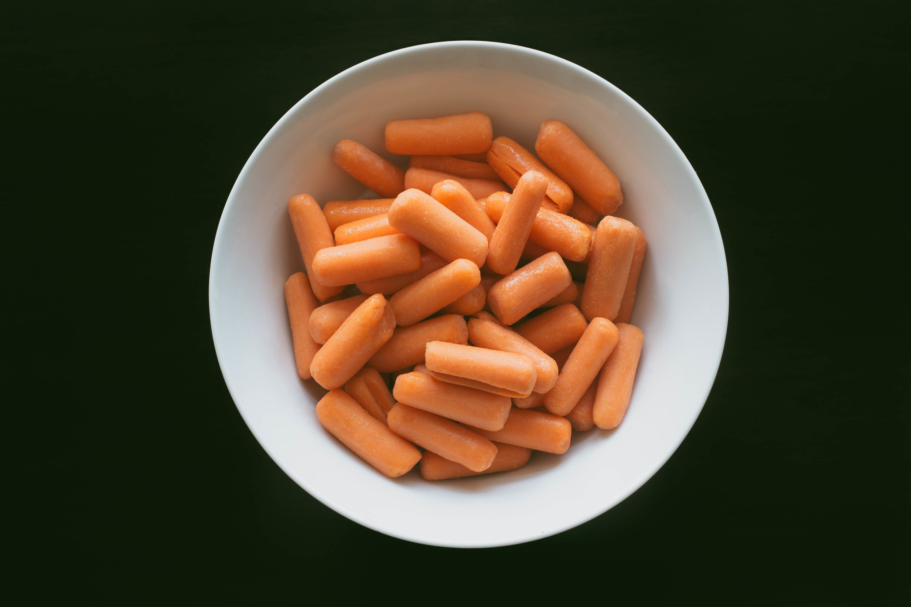 High angle view of baby carrots in bowl on dark background