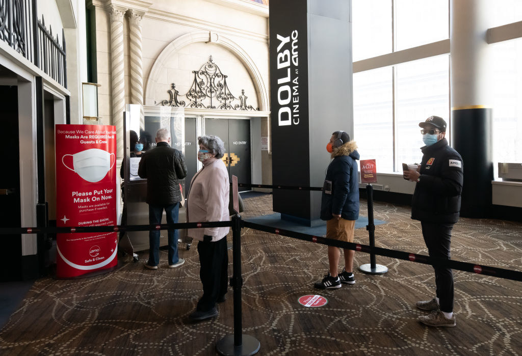 Moviegoers standing at a social distance from one another in line while wearing face masks