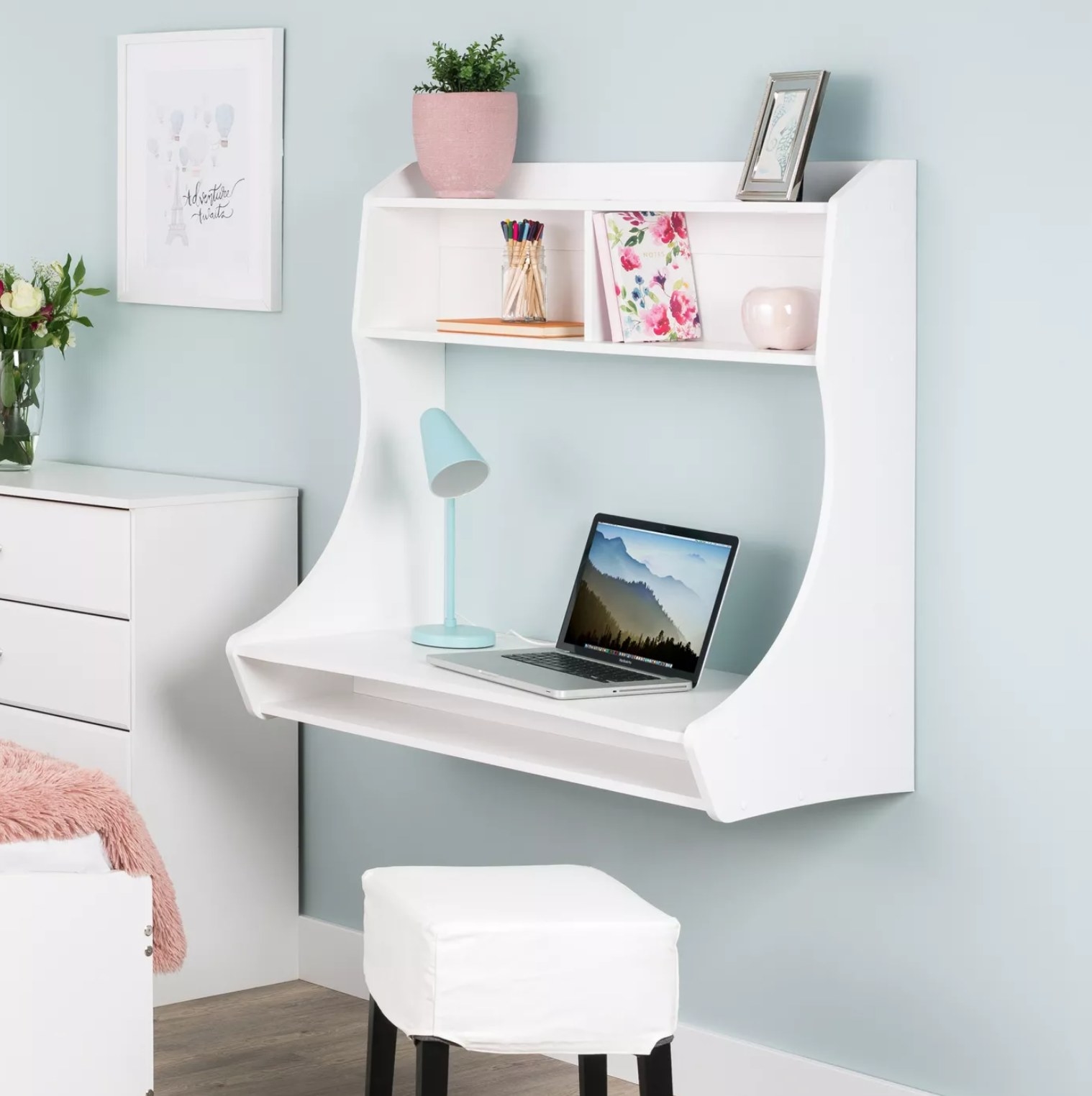 The white wall-mounted desk with a laptop and lamp on it
