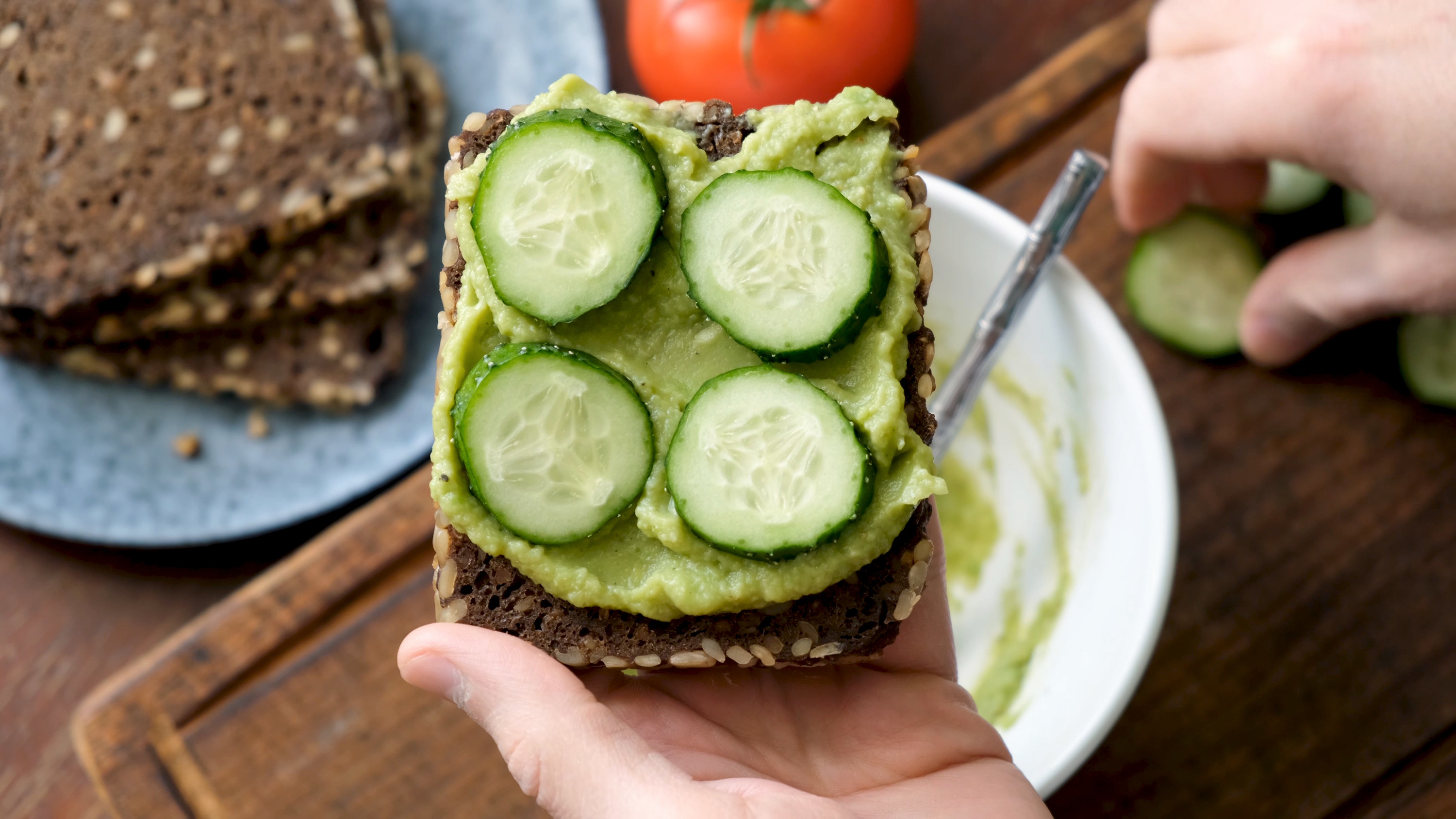 Cucumber and avocado on a slice on bread in someone&#x27;s hand 