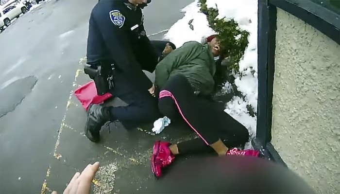 A Black woman is restrained on the ground by a police officer