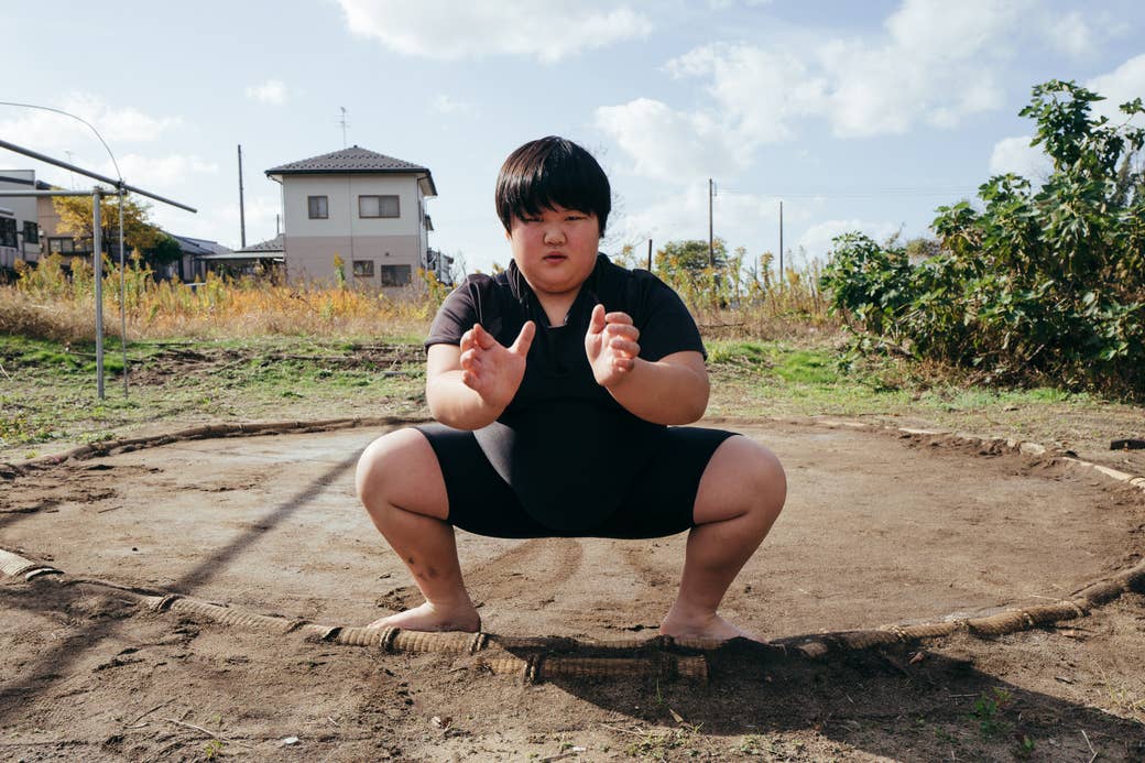 A young female sumo  wrestler squats at the edge of a homemade ring