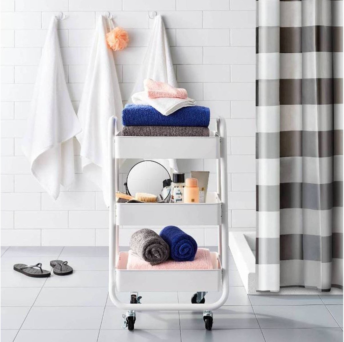 white three-shelf metal cart with wheels and bathroom accessories on the shelves