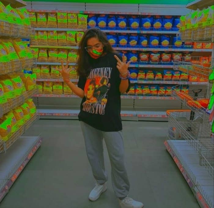 A high contrast image of my sister at the supermarket wearing a Whitney Houston t-shirt, grey joggers, white chunky shoes.