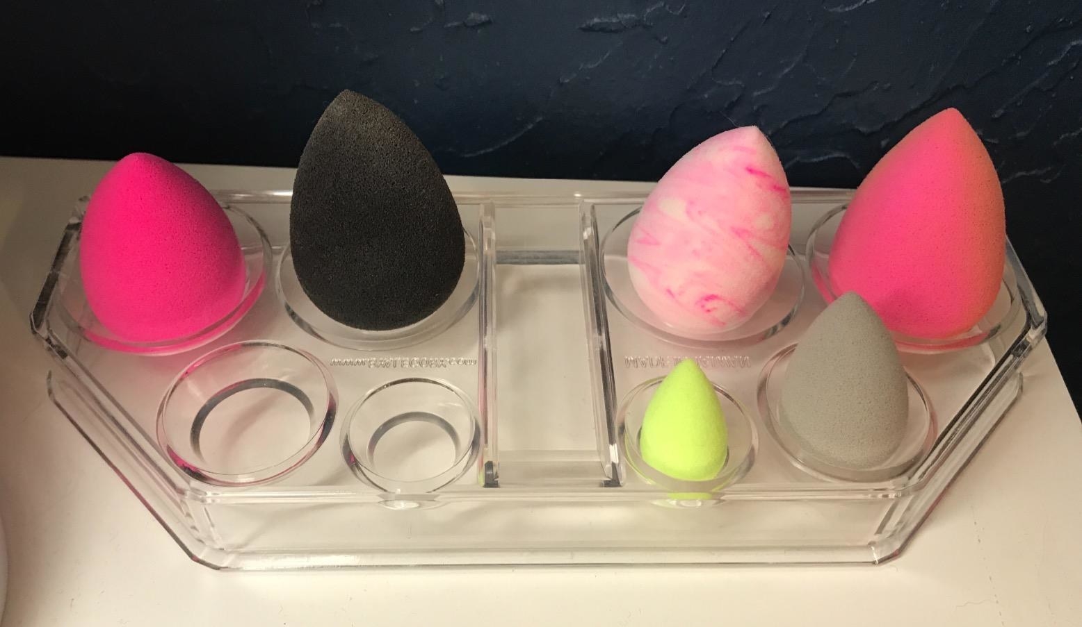 The clear organizer with different size slots holding makeup sponges in different sizes