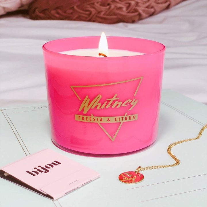 Bright pink candle that says Whitney in gold 