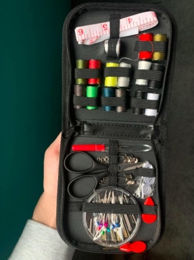 person holding up a sewing kit with different colored threads, scissors, safety pins and other sewing esssentials