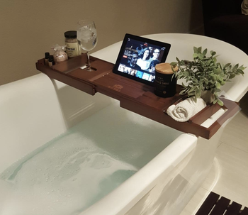 dark wood bamboo caddy positioned over tub holding ipad, candle, and other accessories 
