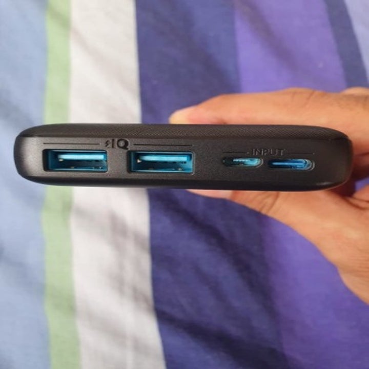 person holding up a portable charger from the side to show the charging ports