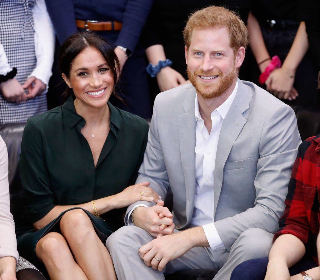 Harry and Meghan holding hands and smiling as they are surrounded by people during an event