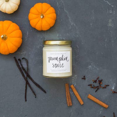 pumpkin spice candle in clear glass jar surrounded by spices and small pumpkin