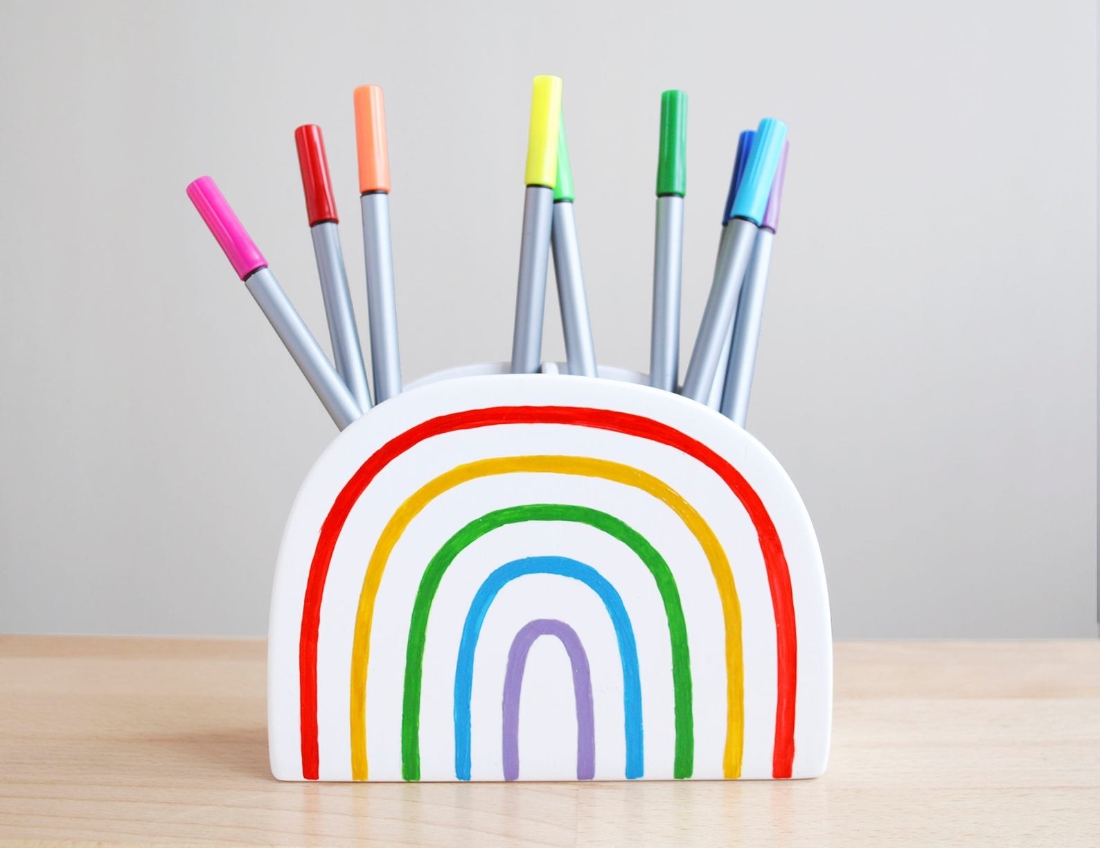 small white ceramic rainbow-shaped pencils holder with openings at the top and colored markers stored in them