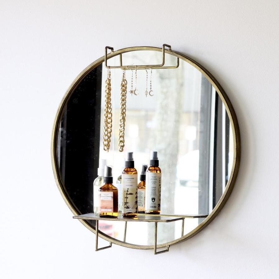 round gold mirror with a gold shelf at the bottom and slim handle at the top