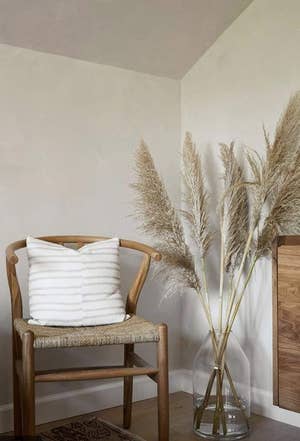 same dried pampas grass in a tall clear vase next to an arm chair