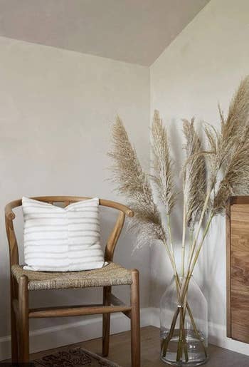 same dried pampas grass in a tall clear vase next to an arm chair