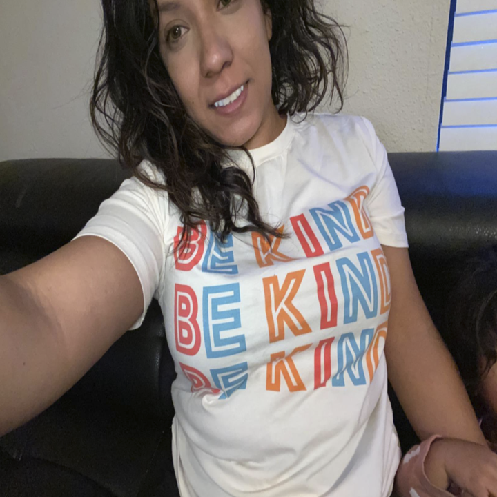 reviewer wearing a white t-shirt that says "be kind" on it it three times in colorful letters