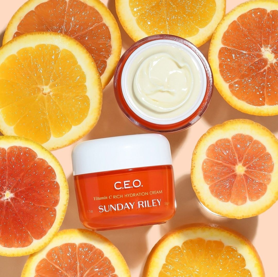 A container of face cream surround by half cut oranges