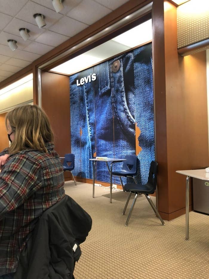 Levi's signage remains up behind school desks, a student in the foreground sits wearing a face mask