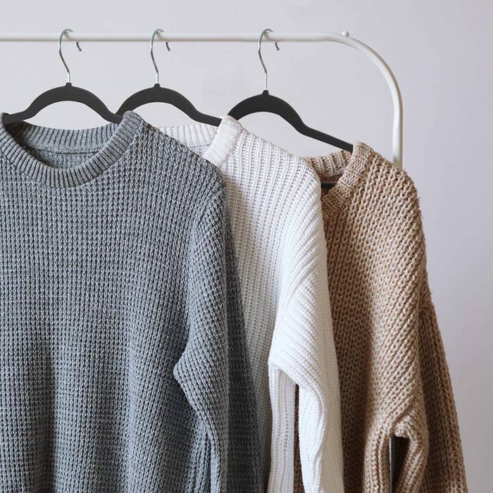 A trio of velvet hangers with sweaters hung on them