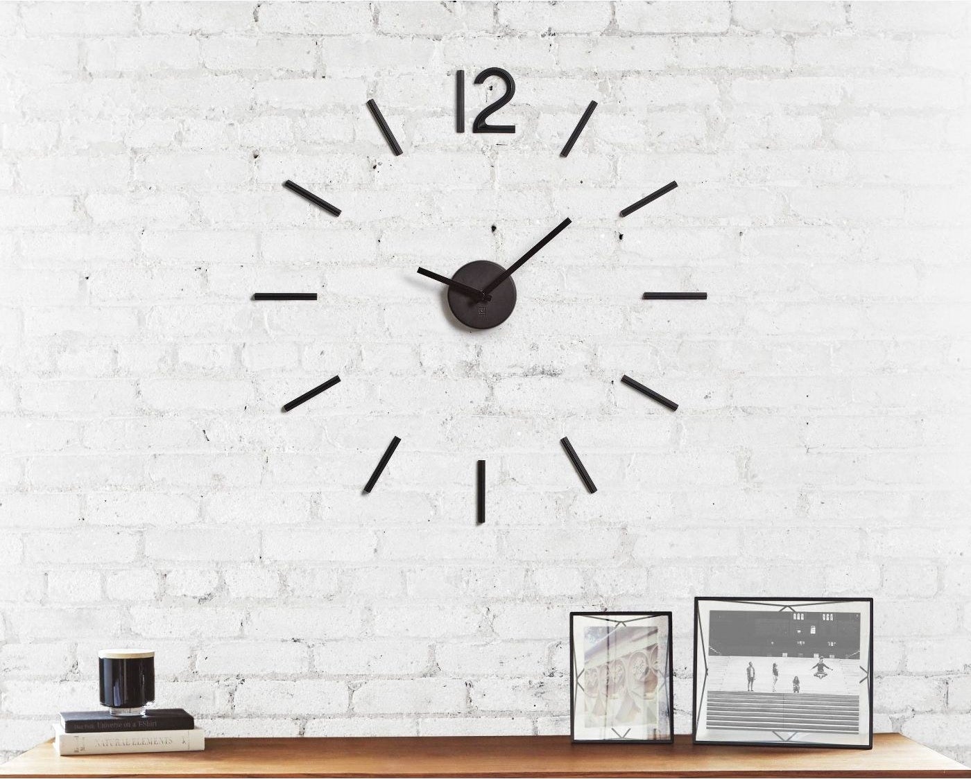 A modern black clock on a white brick wall