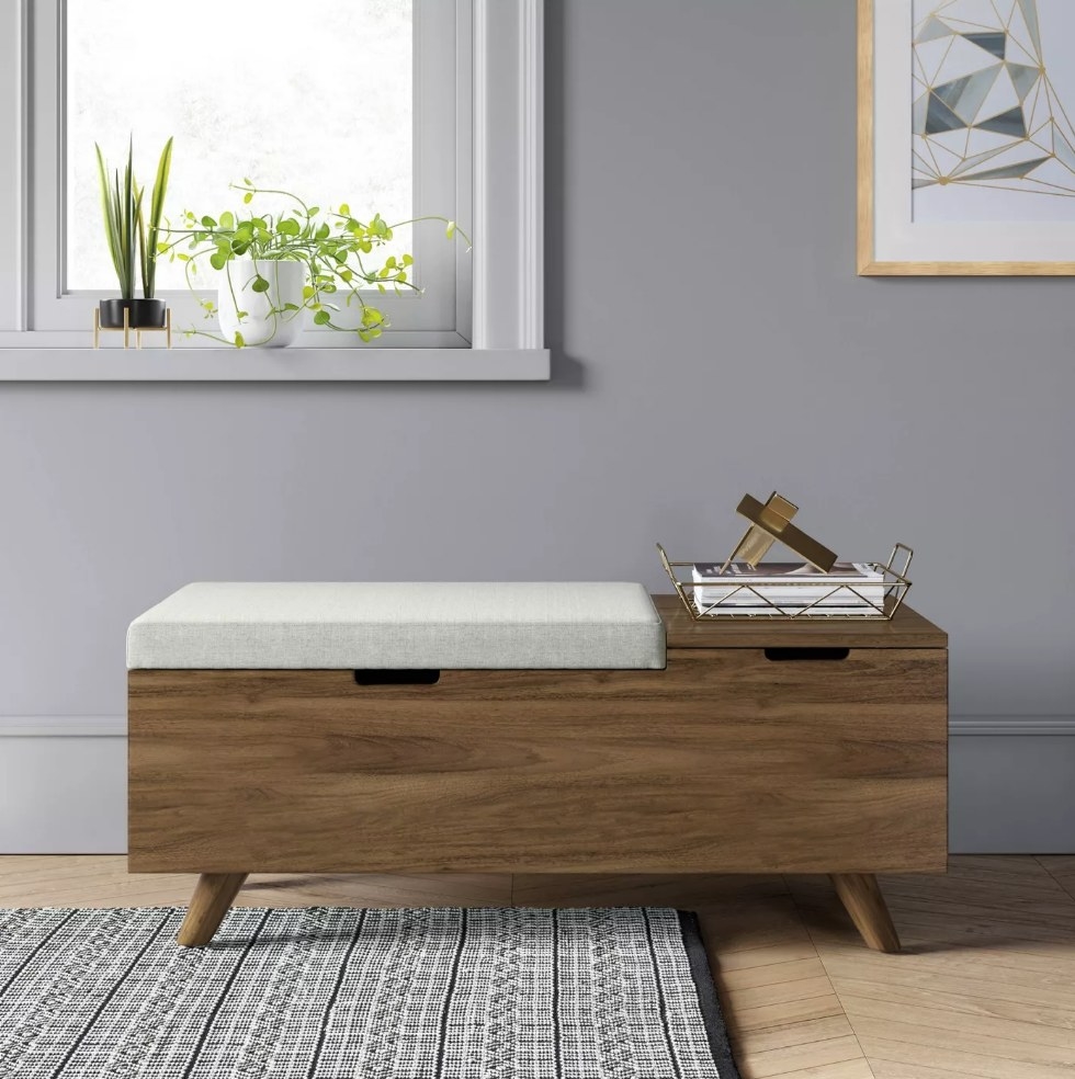 A wooden storage bench with two compartments, one of which has beige padding to sit 