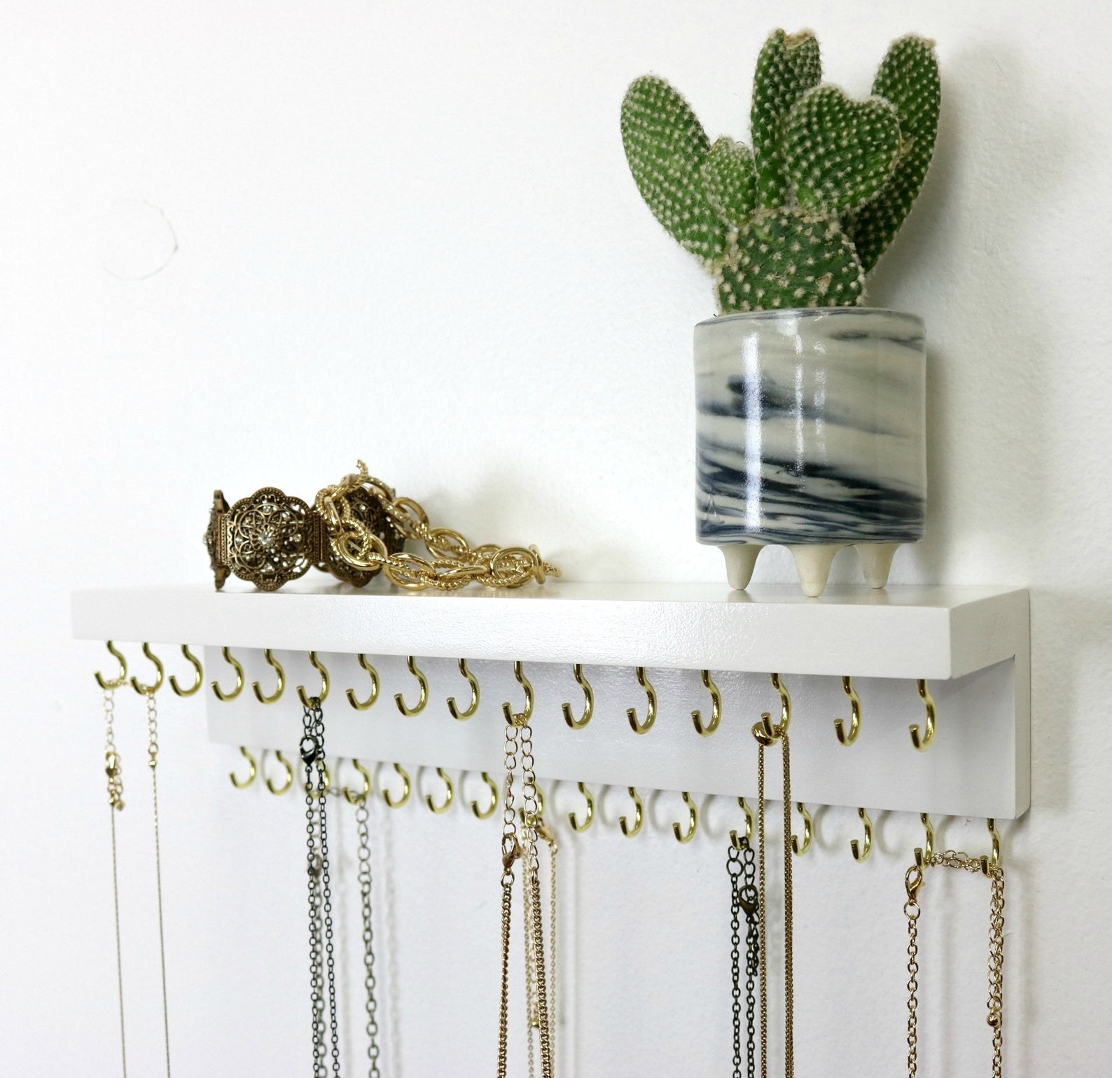white wood shelf with two levels of gold hooks across the bottom