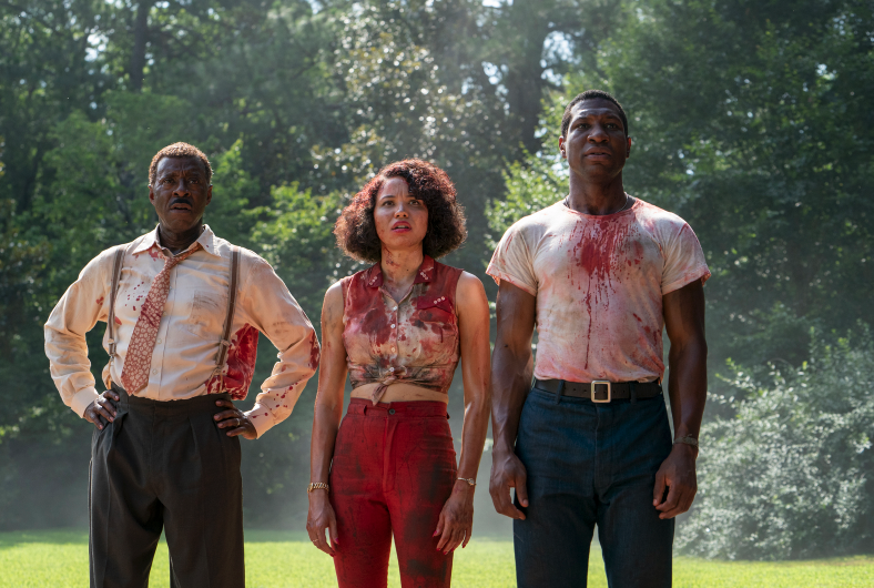 Three people stand side by side, looking in the distance, their outfits covered in blood