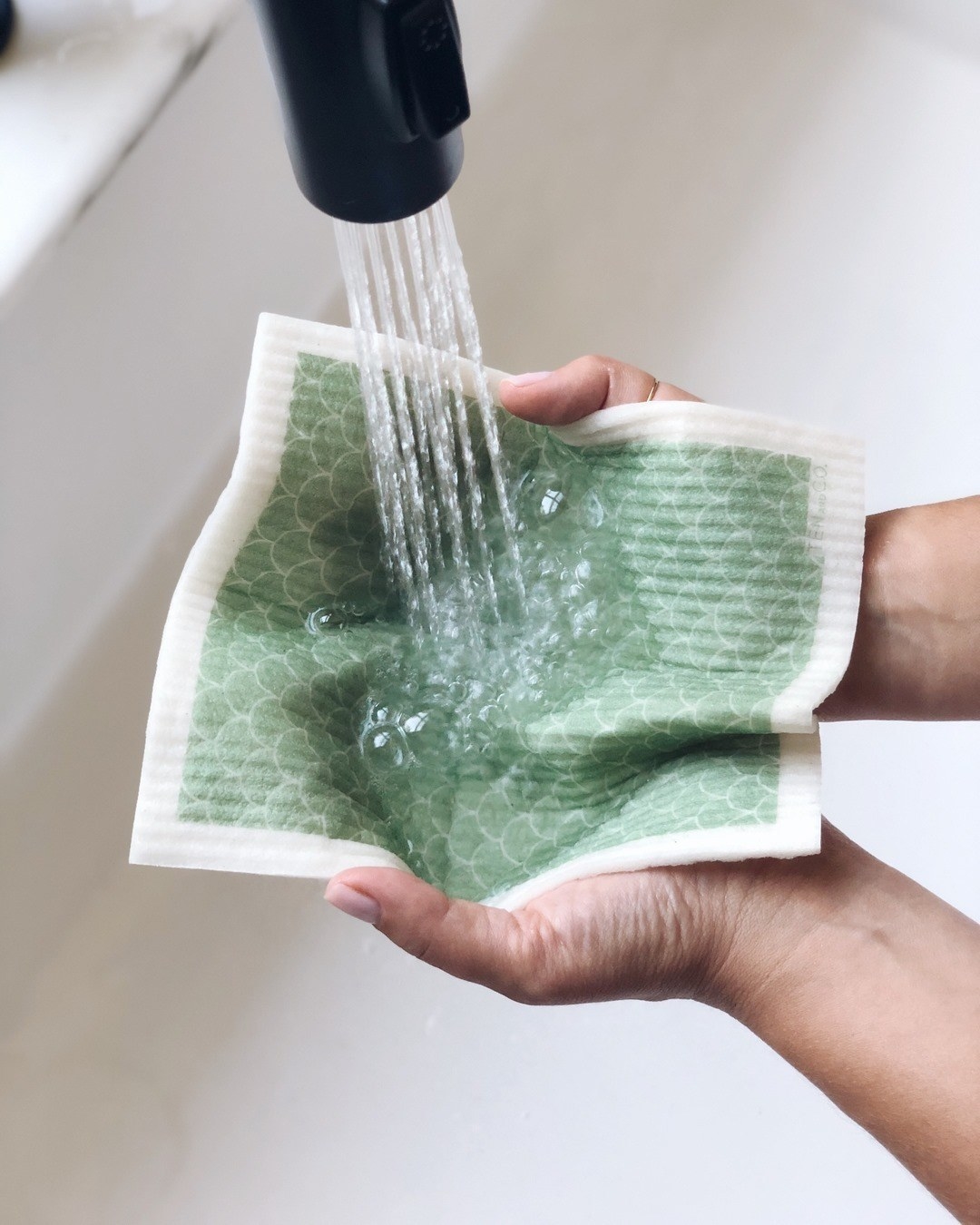 square cloth with green scale-like design in a pair of hands under a faucet