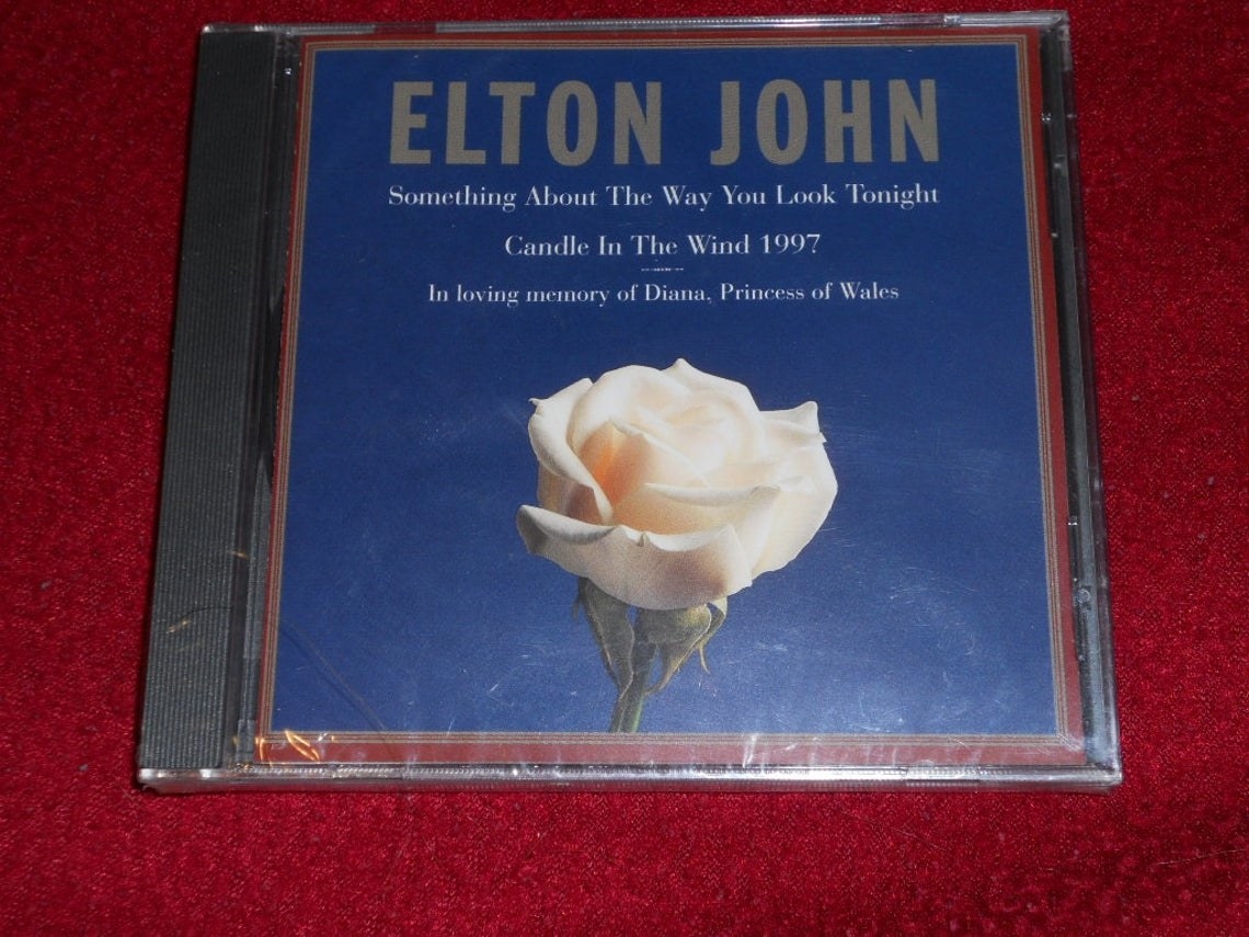 A CD of Candle in the Wind 1997, which features a white rose with a blue background on the cover