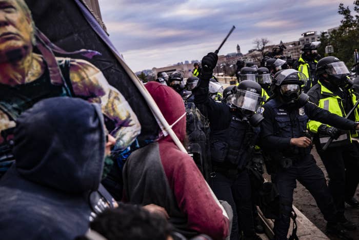 Rioters wearing hoodies and carrying a sign with Trump's head on the movie character Rambo confront officers wearing helmets and face shields and holding clubs