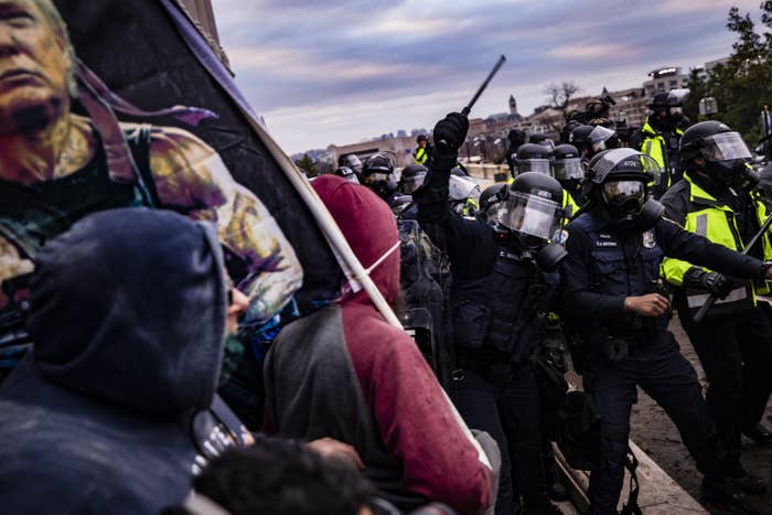 Rioters wearing hoodies and carrying a sign with Trump&#x27;s head on the movie character Rambo confront officers wearing helmets and face shields and holding clubs