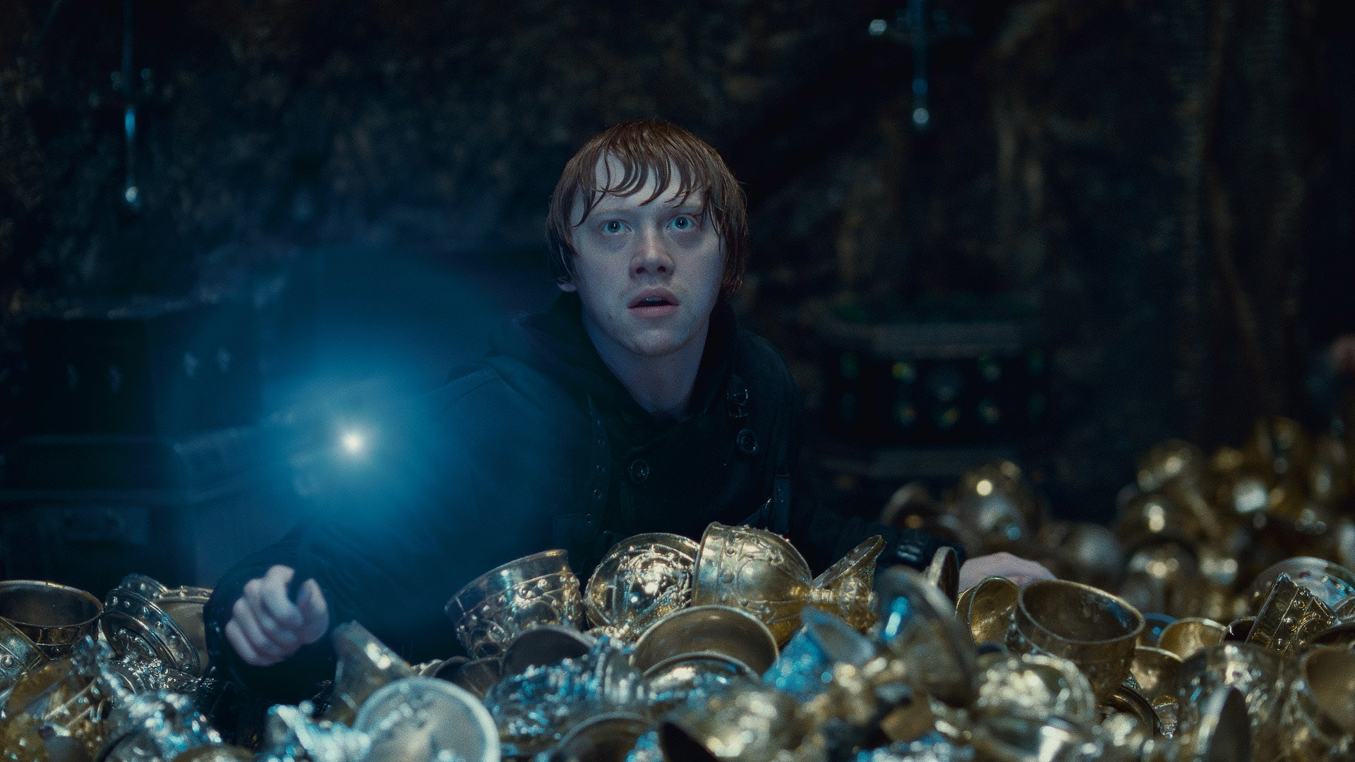 Rupert Grint holds a glowing wand amidst gold cups in Harry Potter and the Deathly Hallows: Part 2