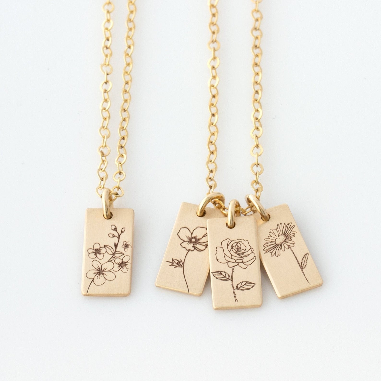 two gold necklaces with rectangular charms on them with flowers on each charm