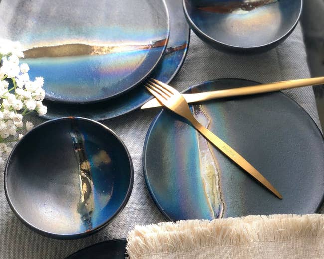 the complete black dinner set with blue and hold metallic luster on a table set with gold utensils