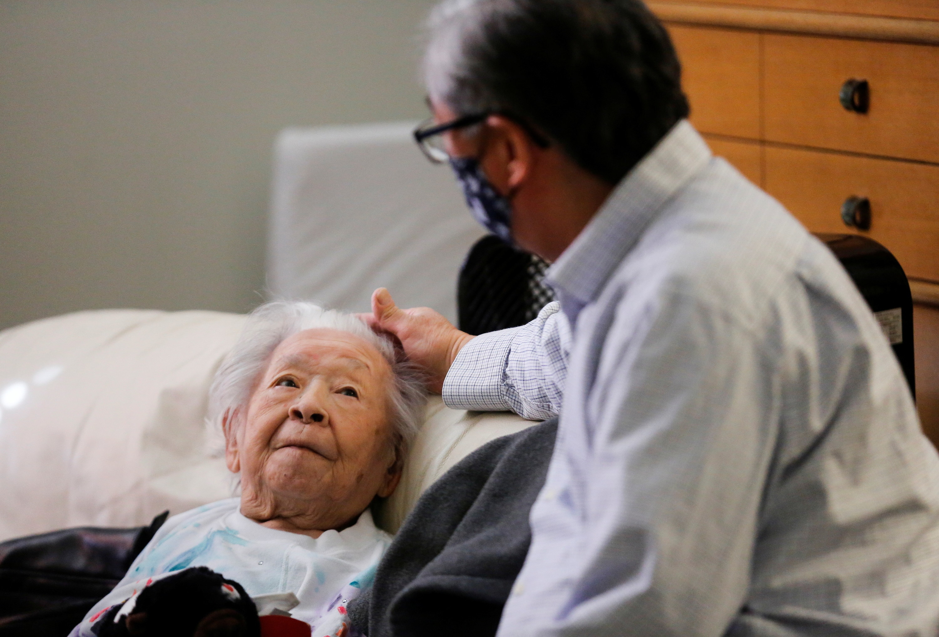 Mark caresses his mother&#x27;s forehead as she stares up at him