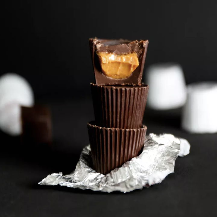 Three dark chocolate peanut butter cups, one broken open so the inside is visible