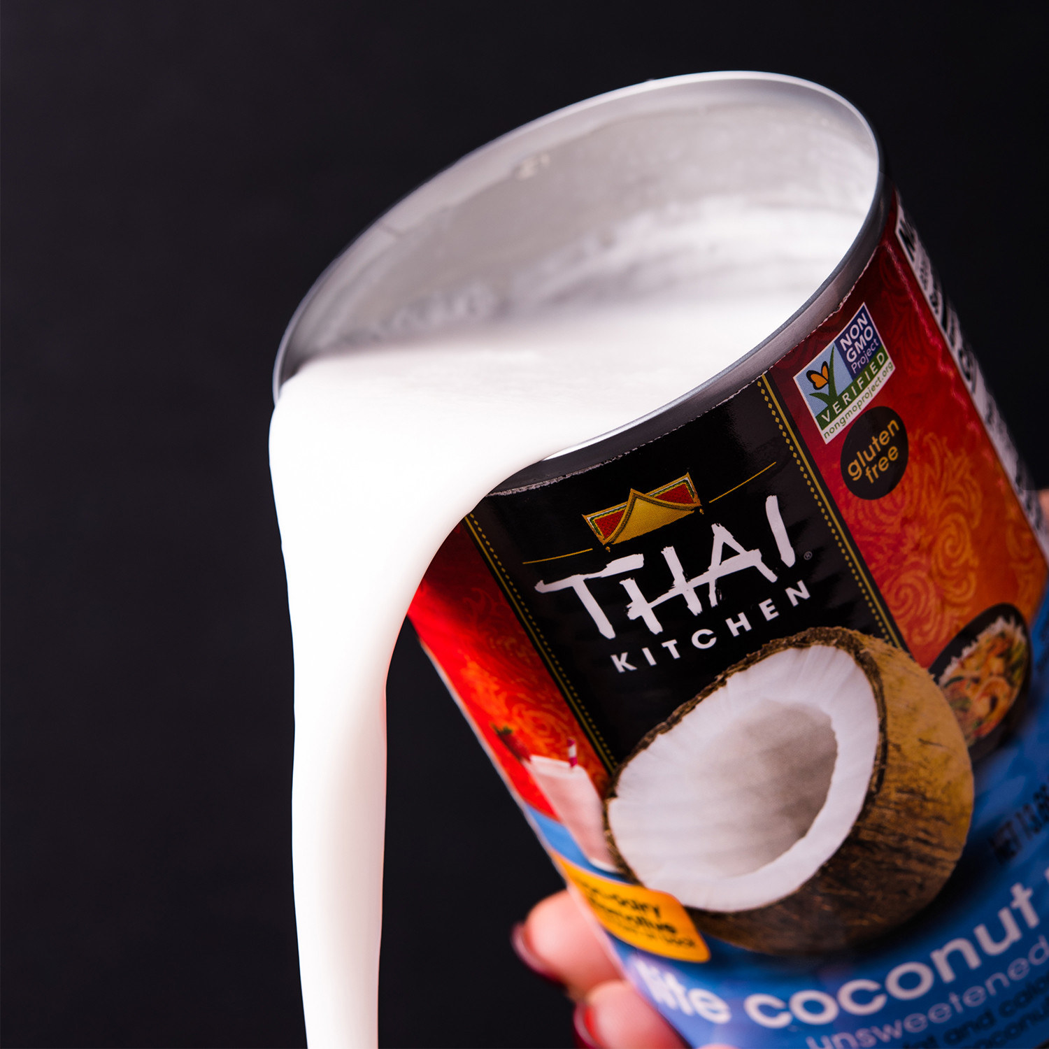 a hand pouring some coconut milk from the can