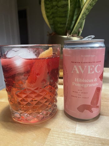 writer's can of hibiscus and pomegranate AVEC next to a red cocktail garnished with orange