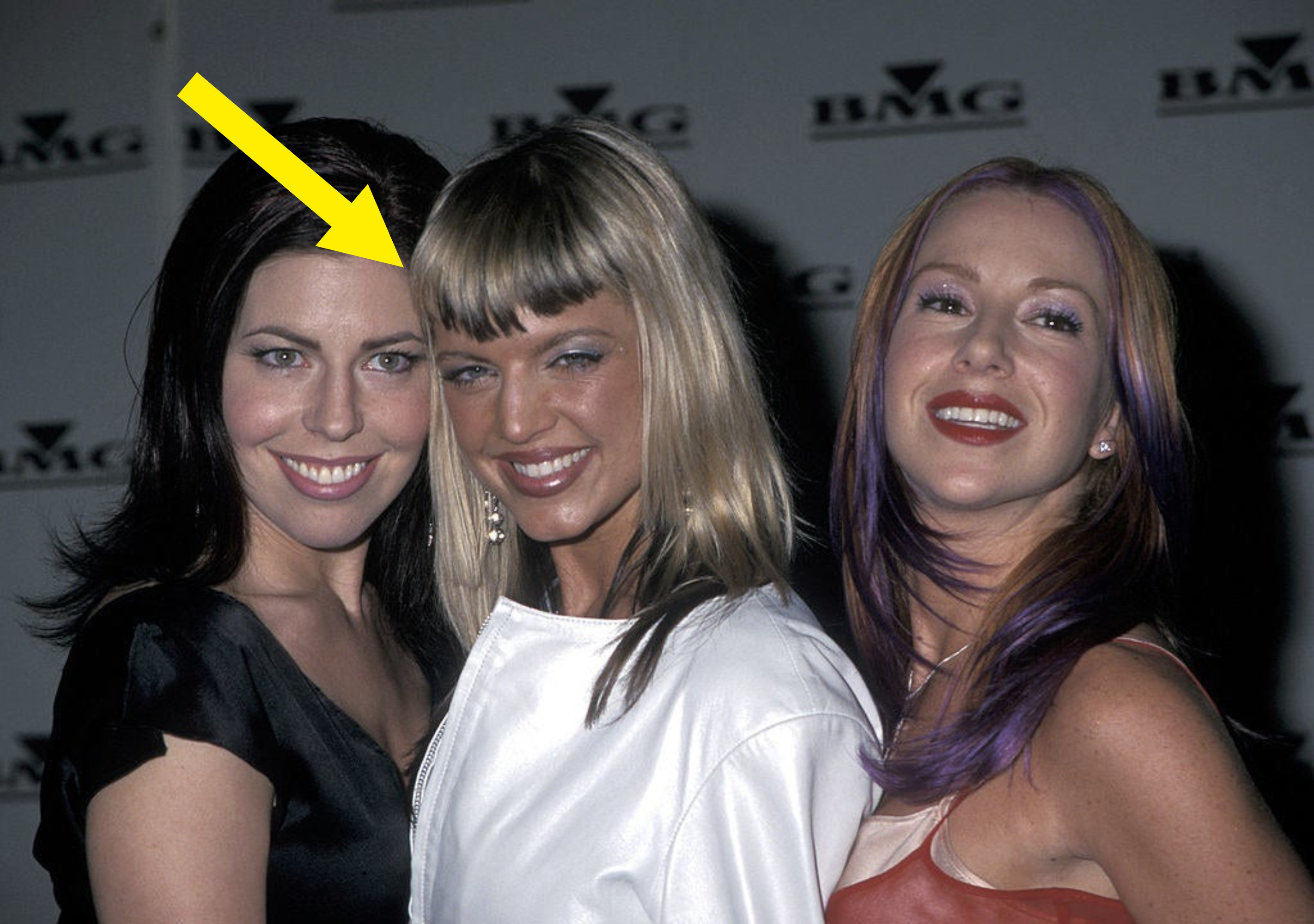 Fergie with a blonde bob and in a white jacket between two other girls at a red carpet 